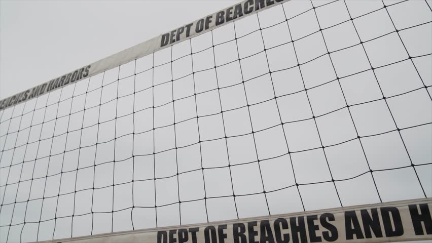This slow motion video shows a young, fit caucasian woman spiking a volleyball over the net on a cloudy beach.  Perfect for chroma keying composite use.