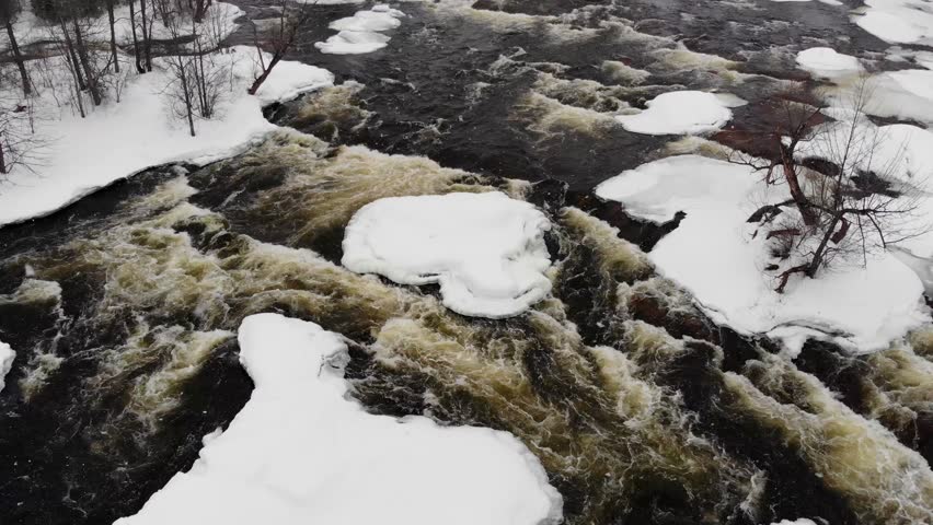 Aerial, tilt up, drone shot, above snowy, Blakeney rapids river, towards a car on a bridge, surrounded by fields and forest, at blizzard, on a winter day, in Mississippi Mills, Ontario, Canada
