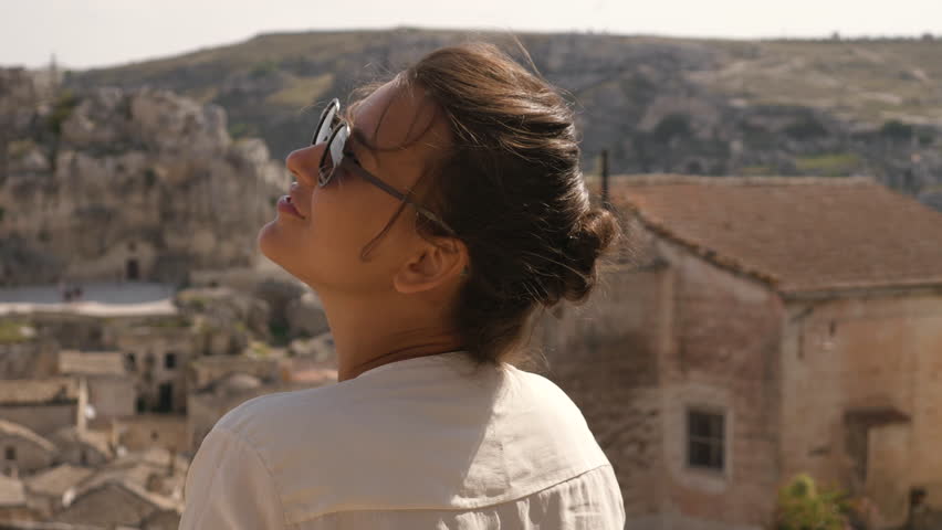 Beautiful elegant young woman in Matera Italy on a high balcony viewpoint with landscape. Fashion dress with hat and skirt. 17