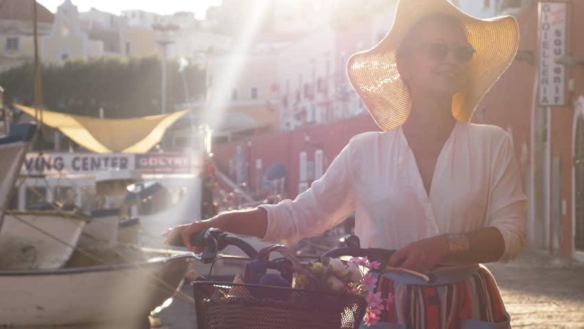 Young woman with vintage bike walking at seafront by the harbor in Ponza island Italy. Fashion colorful dress skirt and hat.