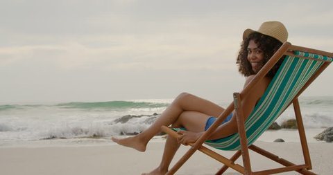 Side view of African american woman relaxing in a sun lounger on the beach. She is smiling an looking at camera.