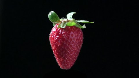 juicy red strawberries with green leaves on an isolated black background rotates in the air