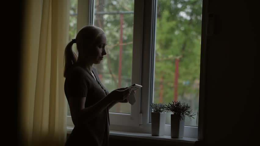 Standing at the window, a woman holding a picture in a frame, looking at her and stroking his hand. | Shutterstock HD Video #1028667302