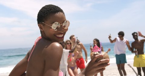Front view of African American woman dancing on the beach. Male and female friends dancing in the background