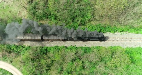Historic train with steam locomotive and old carriages runs on the tracks in the countryside. Aerial view.