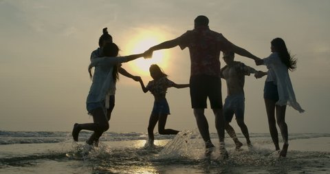 Group of happy friends guys and girls playing in water at beach party on sunset. People with travel, holiday and party concept. Slow motion.