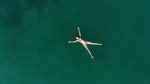 Relaxed woman lie on sea water with arms and hands stretched out, camera fly up, nobody around. Warm and calm waters of Aegean Sea, female swimmer take rest