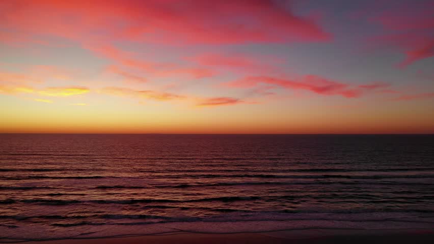 Aerial drone view over the ocean at sunset with neon pink clouds across the dreamy sky. | Shutterstock HD Video #1028706875
