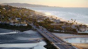 Aerial drone video over Del Mar, facing south down the coastline at sunset, along the low tide shore.