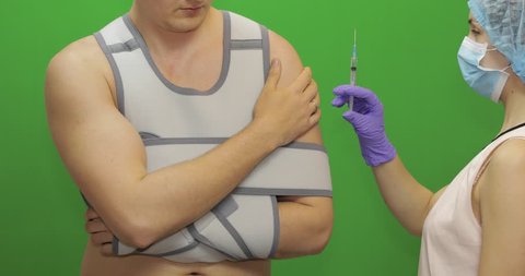 Man with shoulder injury. Nurse with syringe with medicines makes prick from pain. Patient in a bandage for fixing of an elbow joint and a humeral belt. Dislocations of arm of the forearm, shoulder