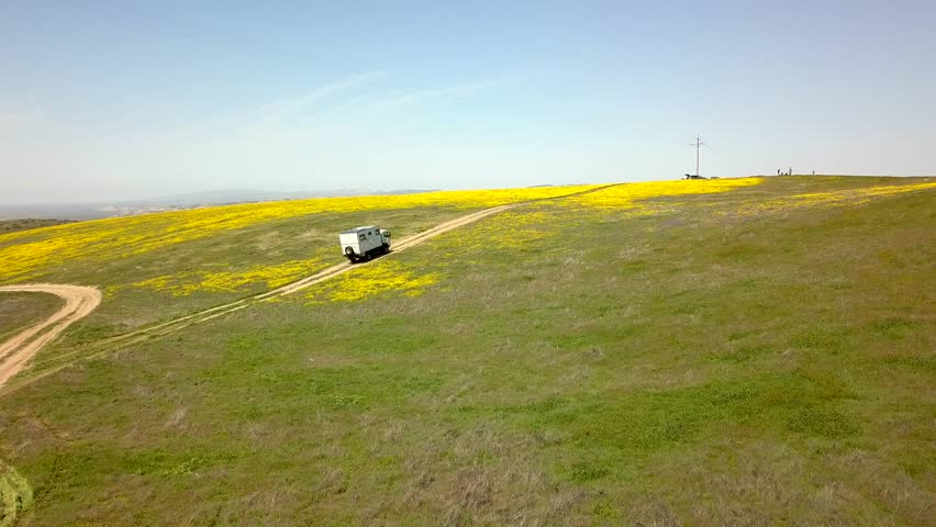 Aerial, drone shot following a camper van, on a dirt road, surrounded by blooming wildflowers, on a sunny spring day, in Carrizo Plain, California valley, USA at SUPER BLOOM