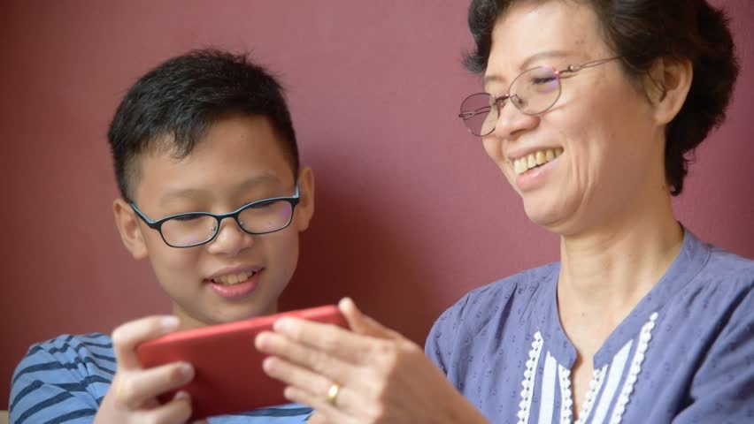 Young asian boy playing games on smartphone with his grandma at home