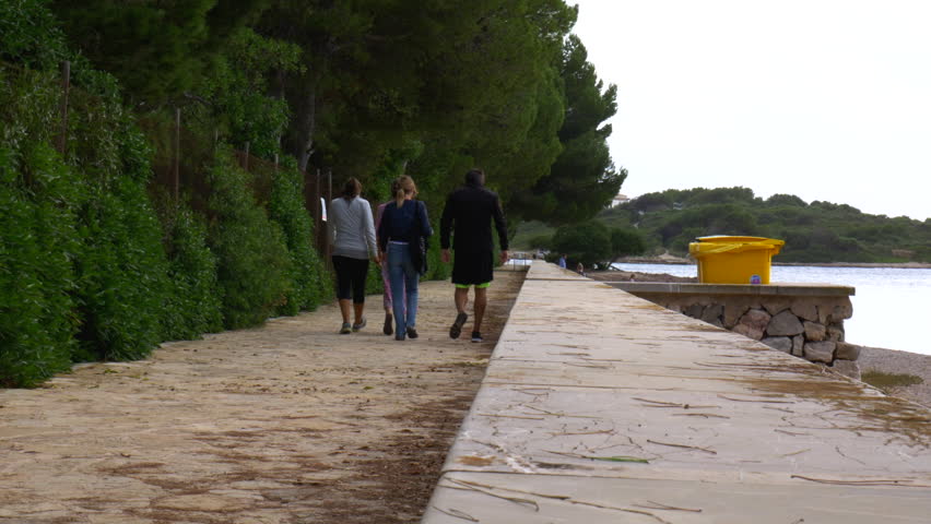 A group of people strolling down the promenade with the water on their right side and an island infront of them. No camera movements. Filmed in realtime at 4k.