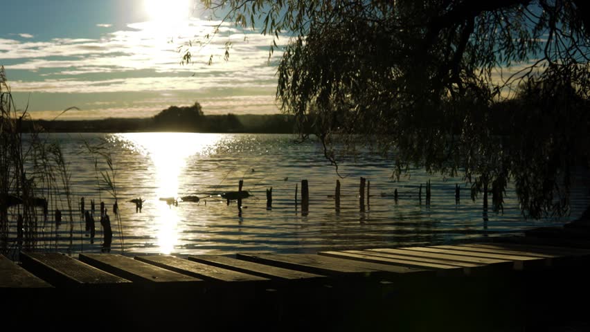 A hazy sunset shot of a man walking on a small wooden bridge over the water.