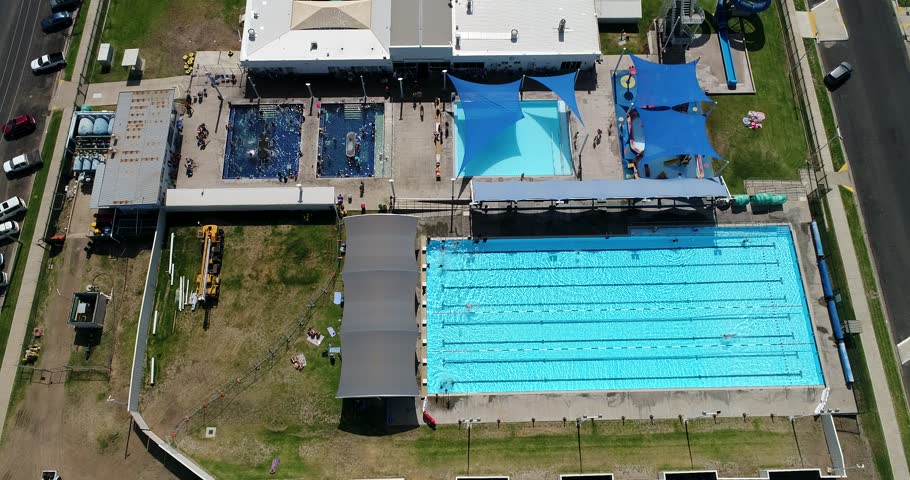 Swimming pools and spa complex of aquatic centre in Moree town – aerial flying away over town streets looking top down to the grounds.
