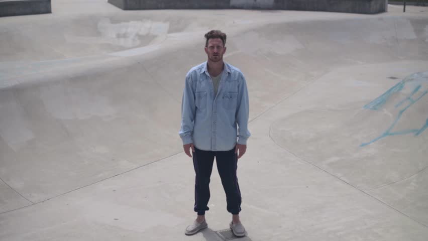 Male movement artist standing inside a skatepark pool, facing the camera. Slow motion shot.