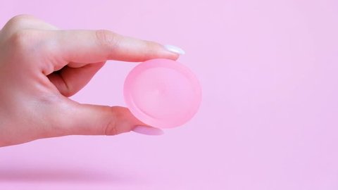 Woman hand  holding menstrual cup. Pink menstrual cup on color background. Alternative feminine hygiene product during the period. Zero waste concept 