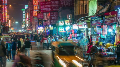 Delhi, India - February 17, 2019: Night time lapse view of busy Main Bazaar street showing neon signs, shops, traffic and pedestrians in central Delhi, India. Dolly right to left.