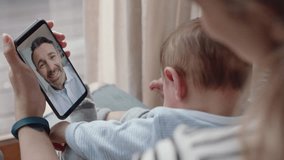 young mother and baby having video chat with father using smartphone waving at little daughter enjoying family connection