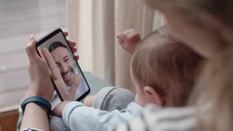 young mother and baby having video chat with father using smartphone waving at little daughter enjoying family connection