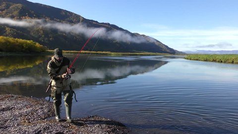 Fishing by means of spinning on the rivers on the Kamchatka Peninsula. Russia, September 2018. A man with a carbine on his back lets go of a fish caught fishing.