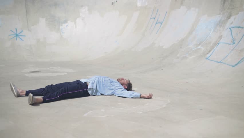 Male movement artist practicing ground transitions and contemporary dance moves inside a skatepark pool. Slow motion shot.