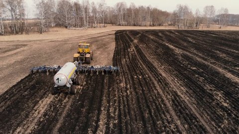 Tractor trailer with liquid ammonia fertilizes the land with wheat. The drone gradually flies toward a moving tractor.