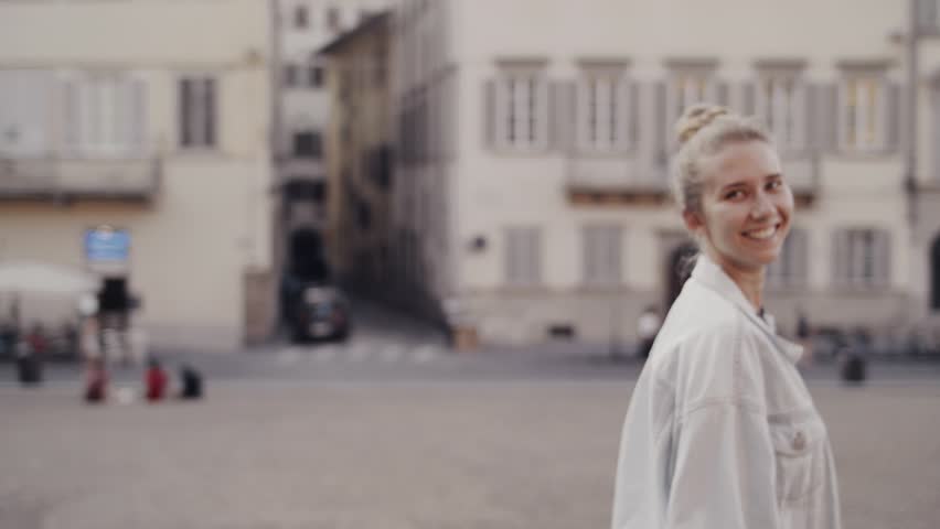 Cheerful young  woman walking in the summer Italian city streets. Black dress and white jeans jacket.  Sunset lightning.