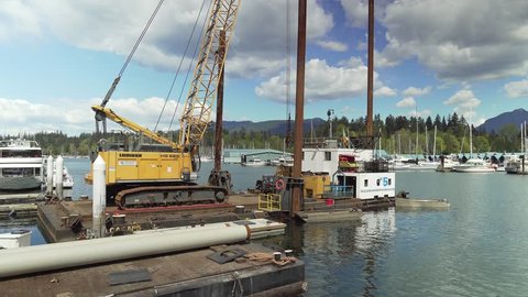 Vancouver, Canada - April 29, 2019. Dock building crew use a crane to position pilings to extend the dock in the Coal Harbour Marina for the summer tourist  whale watching season. 