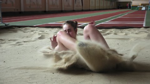 Girl athlete performing long jump into sandbox. Training before the competition. Woman athlete performing long jump in the sports complex. Close-up slow motion video.
