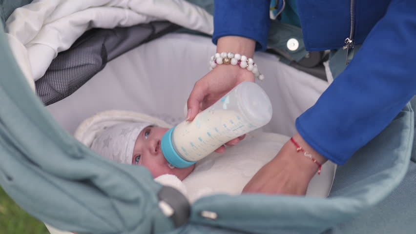 Mother feeds baby boy toddler child milk from a plastic bottle with a bright blue nipple - Caucasian white child with a parent