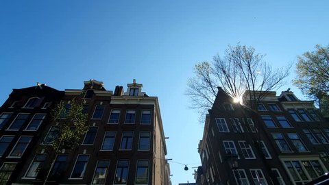 Magnificent architecture of Amsterdam houses. The houses are tilted in different directions. The facades of the houses of Amsterdam on a Sunny day. Glare of the sun shining into the camera