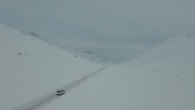 4K drone footage of car driving in snowy landscape.