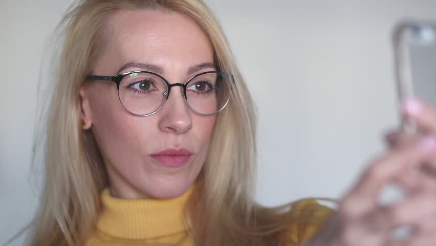 Close up portrait of young attractive blonde female in stylish outfit making a selfie.