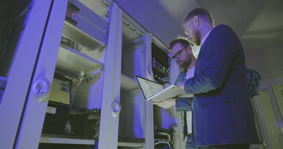 two geek technicians discuss data on screen of laptop. Coders work at modern data center. Royalty-Free Stock Footage #1028761544