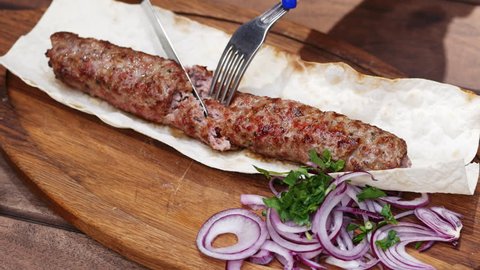 Close-up of grilled lula kebab, traditional oriental dish, woman cuts with knife and fork in restaurant