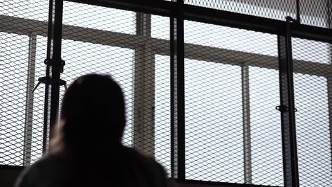 Silhouette Behind Woman Look at Outside Through Lock Up Steel Mesh Window at a Psychiatric Ward