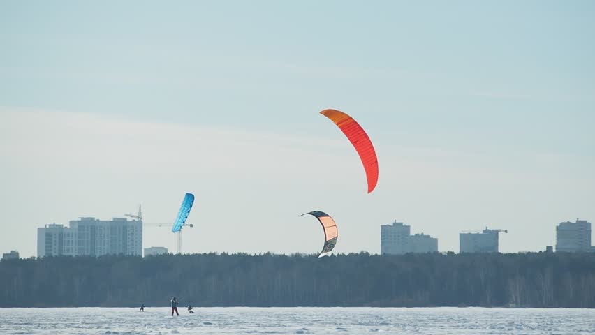 Paragliding In Winter Above Frozen Lake.  Extreme Sport,  Healthy Lifestyle And Freedom Concept. People paragliders training, sunny and windy weather, blue sky. 