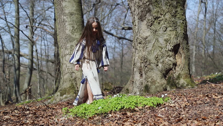 A little girl in the woods picks up a whisk of white forest flowers, and puts it on his head