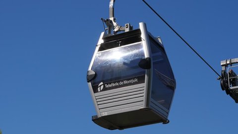 BARCELONA, SPAIN - AUGUST 15, 2018: Empty cabin of Montjuic Cable Car slowly move against blue sky. Modern transportation system at Barcelona, closed booth hang on moving steel cable