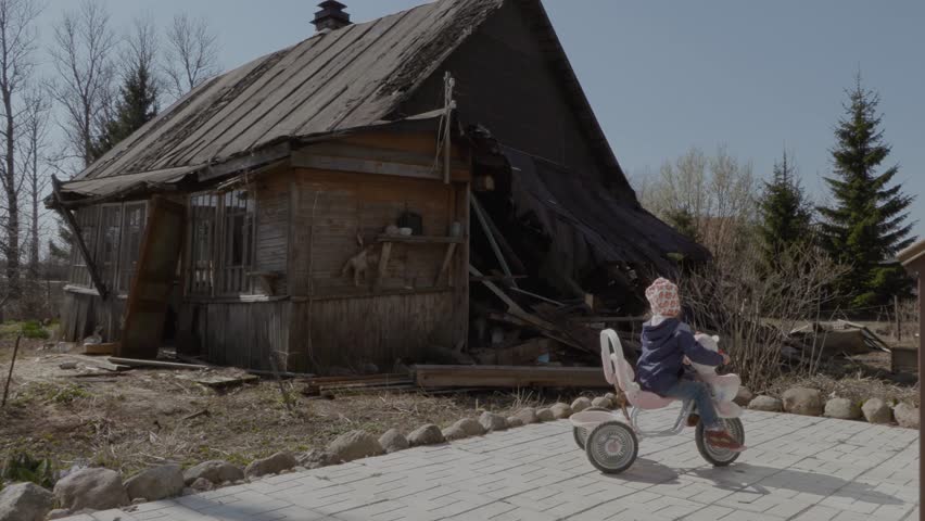little girl on a bicycle on the background of an old wooden house