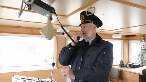 Bearded captain of ship setting radio on captain bridge. Navigation officer manage devices on navigation panel and dashboard in modern ship. Sailing and shipping concept