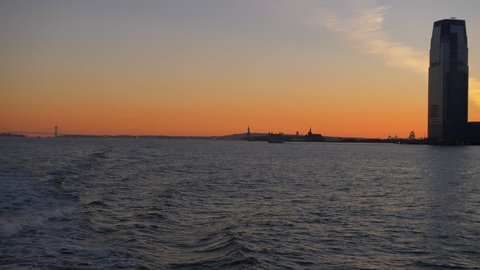 Beautiful Silhouette Of The Statue Of Liberty At Red Sunset.New York City Skyline From Hudson Manhattan Ferry, USA. Establishing Shot. Beautiful Colourful Sky At Night Time. Tourist Attraction