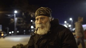 1080p video of an old man with white beard, a khaki bandana on his head and rings on his hands, smoking a pipe