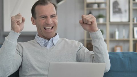 Middle Aged Man Celebrating Success on Laptop at Creative Office