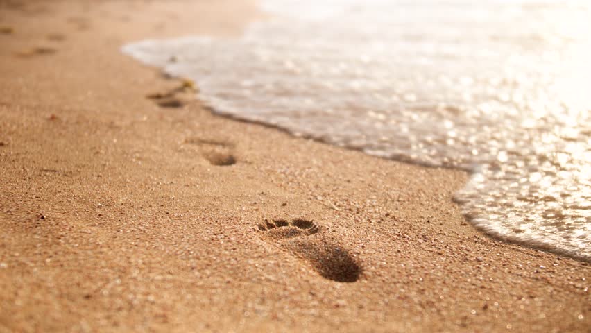 4k closeup footage of sea waves wahing off footprints on the golden sand at beach