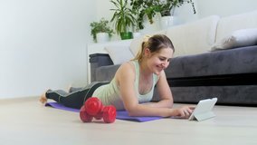 4k footage of young woman exercising on floor a thome. She is watching how to do exercises oand stretching on tablet computer