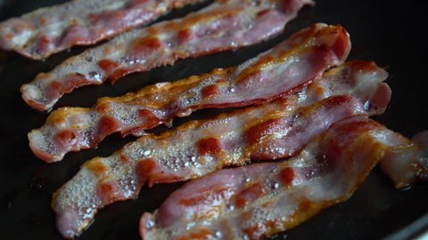 Crispy and thin bacon, rich in fat and colour, sizzling and smoking in a hot pan.