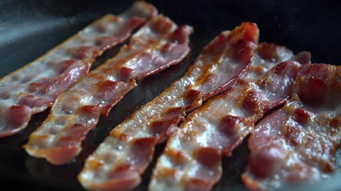 Crispy bacon, rich in fat and colour, sizzling and smoking in a hot pan.