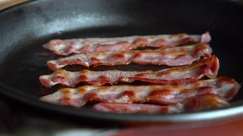 Crispy bacon, rich in fat and colour, sizzling and smoking in a hot pan.